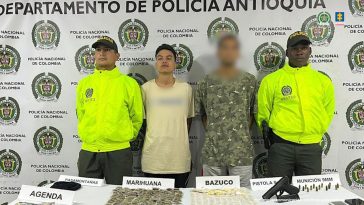 En el centro de la imagen aparece el capturado junto a otra persona con el rostro distorsionado. A cada extremo de la foto aparecen dos miembros de la Policía. En el fondo hay un banner de la Policía.