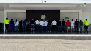 Se visualizan a los capturados de espaldas junto a uniformados de la Policía Nacional. Detrás de ellos el banner que identifica a la Policía Nacional.