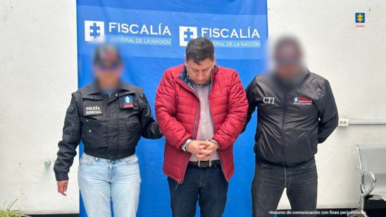 en la fotografía se ve al detenido en medio de dos funcionarios de la Fiscalía, detras de ellos esta un bakin de la Fiscalia