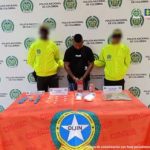 En la fotografía aparece un hombre moreno de pie, con los brazos adelante esposados, cabellos crespos negros, vestido con una camiseta negra y jean azul, custodiado por dos uniformados de la Policía Nacional.