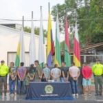 Los capturados se encuentran de espalda y en custodia por uniformados de la Policía Nacional. En la foto se observa una mesa con el estupefaciente que ellos comercializaban y detrás se ven unas banderas.