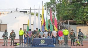 Los capturados se encuentran de espalda y en custodia por uniformados de la Policía Nacional. En la foto se observa una mesa con el estupefaciente que ellos comercializaban y detrás se ven unas banderas.