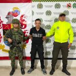 El capturado aparece en el centro de la imagen, con un miembro del Ejército en uno de sus costados y en el otro uno de la Policía. Al fondo aparecen banner de las dos instituciones.