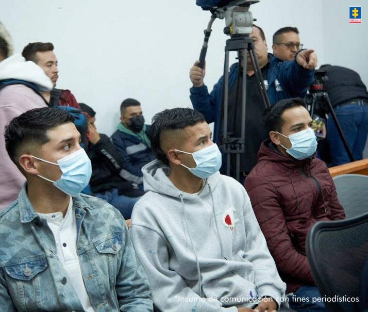 En la imagen se ven tres hombres sentados y con tapabocas sobre sus rostros. Al fondo pueden verse miembros de medios de comunicación.