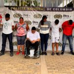 capturados de frente custodiados por policías y militares. Dertrás baner de la Policía Nacional.