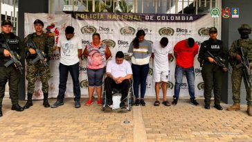 capturados de frente custodiados por policías y militares. Dertrás baner de la Policía Nacional.