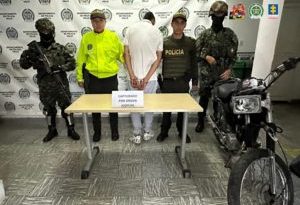 En la fotografía aparece de espaldas a la cámara, de pie, con los brazos atrás y esposado Andrés Felipe Posso. Viste camisa de manga corta de color blanco, jean azul claro y zapatillas blancas con negro. A sus extremos hay uniformados de la Policía y Ejército. Delante de ellos hay una mesa y sobre ella hay un letrero que dice: ‘Capturado por orden judicial’. Al lado de la mesa se aprecia una motocicleta. En la parte posterior hay un pendón institucional de la Policía.