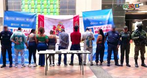 Se observan ocho personas capturadas, de espalda y en fila. A cada costado uniformados del Cuerpo Técnico de Investigación CTI, del Ejército Nacional y de la Policía Nacional. Atrás dos pendones de la Fiscalía General de la Nación y uno del Ejército Nacional. Adelante una mesa con material incautado.