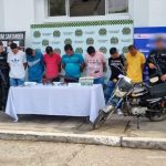 en la fotografia se visualiza los7 miembros del grupo delincuencial, entre 6 funcionarios del ejercito y el CTI de la Fiscalia, en frente de ellos se encuentra una mesa con evidencia que se les incauto al igual que una motocicleta, atras de ellos se ve un baking de la policia, del ejercito y la fiscalia