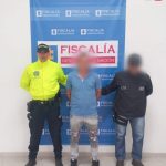 Se observa al capturado de frente, con un efecto que cubre su rostro.  A un costado, un funcionario del CTI y al otro, uno de Policías Nacional.  Atrás, un pendón de Fiscalía General de la Nación