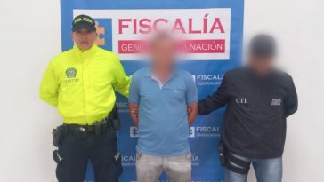 Se observa al capturado de frente, con un efecto que cubre su rostro.  A un costado, un funcionario del CTI y al otro, uno de Policías Nacional.  Atrás, un pendón de Fiscalía General de la Nación