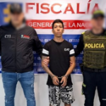 Se visualiza al capturado junto a un investigador del CTI y un uniformado de la Policía Nacional. Detrás de ellos el banner que identifica a la Fiscalía General de la Nación