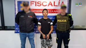 Se visualiza al capturado junto a un investigador del CTI y un uniformado de la Policía Nacional. Detrás de ellos el banner que identifica a la Fiscalía General de la Nación