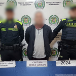 Se visualiza al capturado junto a dos uniformados de la Policía Nacional. Detrás de ellos el banner que identifica a la Policía Nacional.