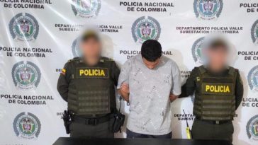 Se visualiza al capturado junto a dos uniformados de la Policía Nacional. Detrás de ellos el banner que identifica a la Policía Nacional