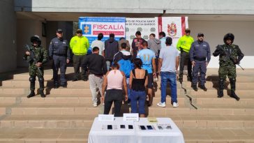 en la imagene se ve a los 12 detenidos de espaldas custodiados por agentes del CTI y la policia, detras de ellos hay un baking de la fiscalia y la policia