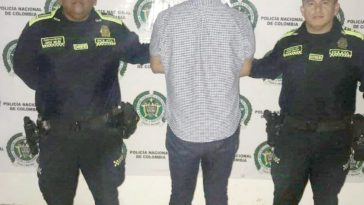 En la imagen se ve al detenido de espalda en medios de dos funcionarios de la policía, detras de ellos hay un baking de la policia