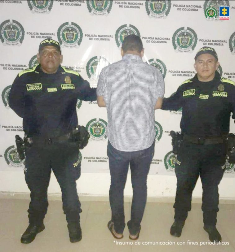 En la imagen se ve al detenido de espalda en medios de dos funcionarios de la policía, detras de ellos hay un baking de la policia