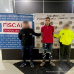 Se visualiza al capturado junto a un investigador del CTI y un uniformado de la Policía Nacional. En la parte posterior los banners institucionales de la Fiscalía General de la Nación y de la Policía Nacional