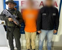 En la fotografía aparece el capturado junto a un funcionario del CTI y un uniformado de la Policía Nacional. En la parte superior está un banner de la Fiscalía General