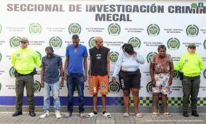 En la fotografía aparecen cinco de los seis capturados junto a dos uniformados de la Sijín de la Policía. En la parte superior está un banner de la Fiscalía General de la Nación