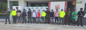 En la imagen se ven varias personas detenidas bajo custodia de varios integrantes del Ejército y la Policía Nacional. Detrás hay varios backings institucionales.