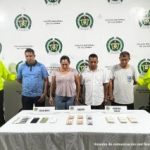 En la imagen se ven tres personas detenidas bajo custodia de la Policía Nacional. Detrás suyo un backing institucional. Delante de ellos varios elementos incautados como bolívares, billetes venezolanos y celulares.