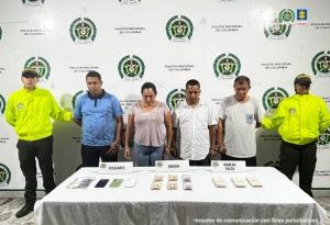 En la imagen se ven tres personas detenidas bajo custodia de la Policía Nacional. Detrás suyo un backing institucional. Delante de ellos varios elementos incautados como bolívares, billetes venezolanos y celulares.