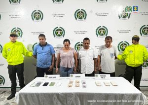 En la imagen se ven tres personas detenidas bajo custodia de la Policía Nacional. Detrás suyo un backing institucional. Delante de ellos varios elementos incautados como bolívares, billetes venezolanos y celulares.