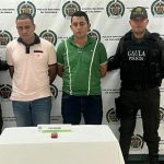 En la imagen aparecen dos personas, una de suéter rosado y otro verde, entre dos uniformados de la Policía.