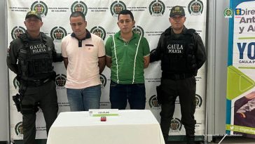 En la imagen aparecen dos personas, una de suéter rosado y otro verde, entre dos uniformados de la Policía.