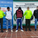 Se visualiza a los capturados junto a uniformados de la Policía Nacional e investigador del CTI. Detrás los banners que identifican a la Fiscalía General de la Nación y a la Policía Nacional. --