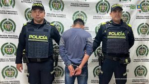 El capturado aparece  de espalda a la cámara, está custodiado por uniformados por uniformados de la Policía.