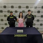 La mujer capturada se encuentra de frente y custodiada por dos uniformados de la Policía Nacional. Detrás hay un backing de la Policía.