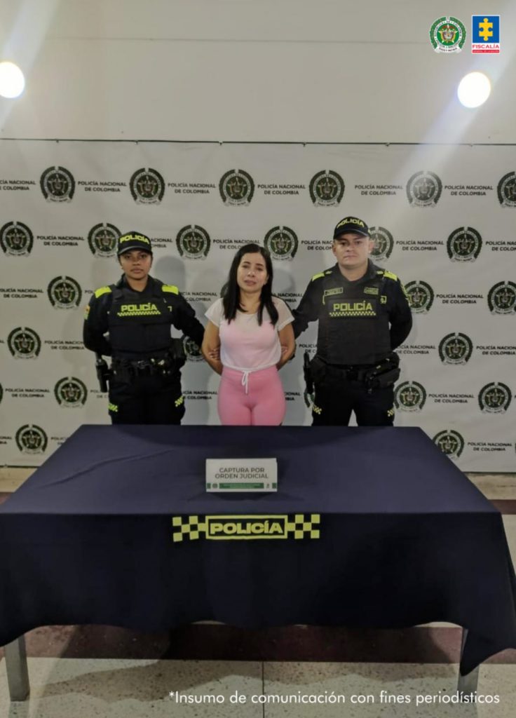 La mujer capturada se encuentra de frente y custodiada por dos uniformados de la Policía Nacional. Detrás hay un backing de la Policía.