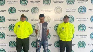 La persona capturada es vista de frente. A cada lado un agente de la Policía Nacional y detrás una pancarta de la Policía Nacional