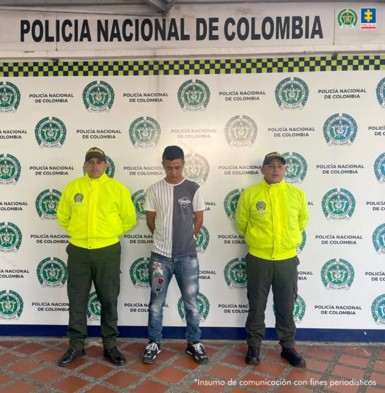 La persona capturada es vista de frente. A cada lado un agente de la Policía Nacional y detrás una pancarta de la Policía Nacional