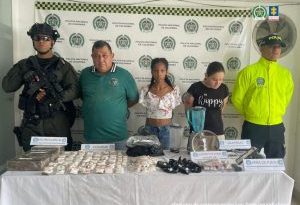 Se observan tres personas capturadas, en fila y de frente. A cada costado de la fila, un funcionario de la Policía Nacional. Atrás un pendón de Policía Nacional. Adelante una mesa en donde se observan las sustancias estupefacientes y otros elementos incautados en las diligencias de allanamiento y registro.