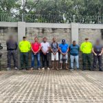 En la fotografía están los procesados de pie con los brazos hacia adelante esposados. Se encuentran acompañados de uniformados del CTI y de la Policía Nacional.