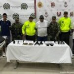 En la imagen aparecen tres personas detenidas, entre uniformados de la Policía Nacional y el Ejército y frente a una mesa con armas y municiones.