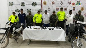 En la imagen aparecen tres personas detenidas, entre uniformados de la Policía Nacional y el Ejército y frente a una mesa con armas y municiones.