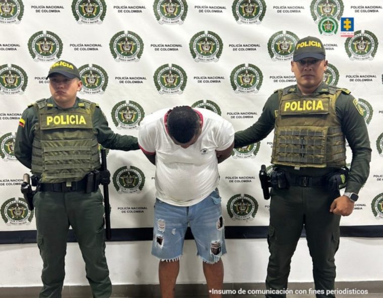 En la imagen aparece una persona de suéter blanco y bermuda de jean, entre dos uniformados de la Policía.