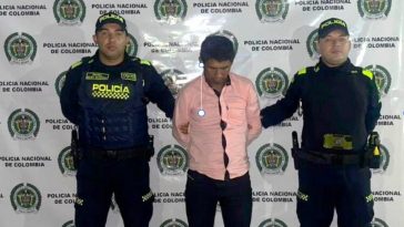 El capturado está esposado, y custodiado por dos uniformados de la Policía Nacional.