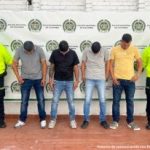 Los capturados se encuentran de frente  y  custodiados por dos uniformados de la Policía Nacional. Detrás se ve un backing de la Policía Nacional.