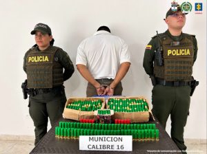 El capturado se encuentra de espalda y custodiado por dos uniformados de la Policía Nacional. En la foto se observa la munición incautada.