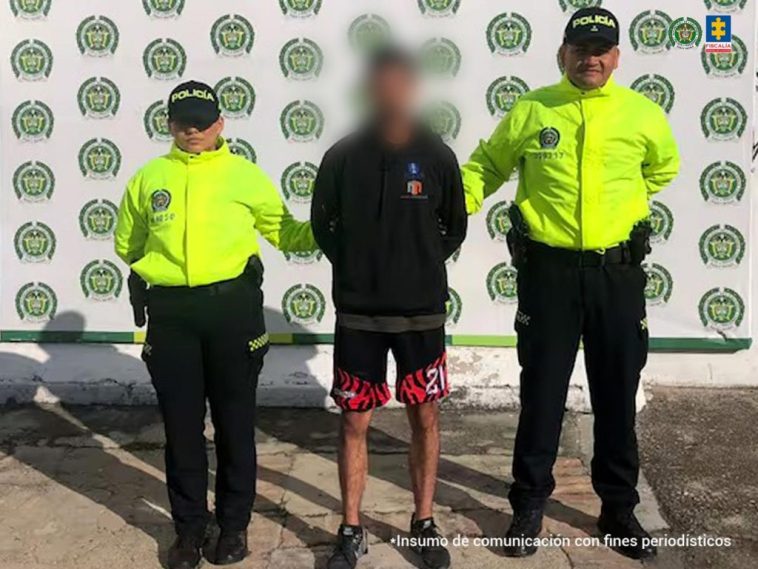 Se visualiza al capturado junto a dos uniformados de la Policía Nacional. Detrás de ellos el banner que identifica a la Policía Nacional en Ocaña (Norte de Santander).