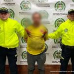 El condenado aparece esposado y custodiado por dos uniformados de la policía nacional.