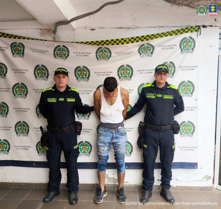 En la fotografía se aprecia de pie, agachado y con los brazos atrás al presunto implicado. Viste camisa esqueleto blanca, jean azul claro desgastado y zapatos azules. A sus extremos hay uniformados de la Policía Nacional. Detrás de ellos hay un pendón institucional de la Policía.