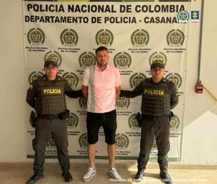 en la imagen se ve una persona detenida bajo custodia de dos integrantes de la Policía Nacional.