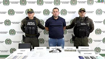 El capturado aparece con sus manos esposadas a la espalda, y se encuentra custodiado por uniformados del Gaula de la Policía Nacional. Detrás de ellos un pendón institucional.